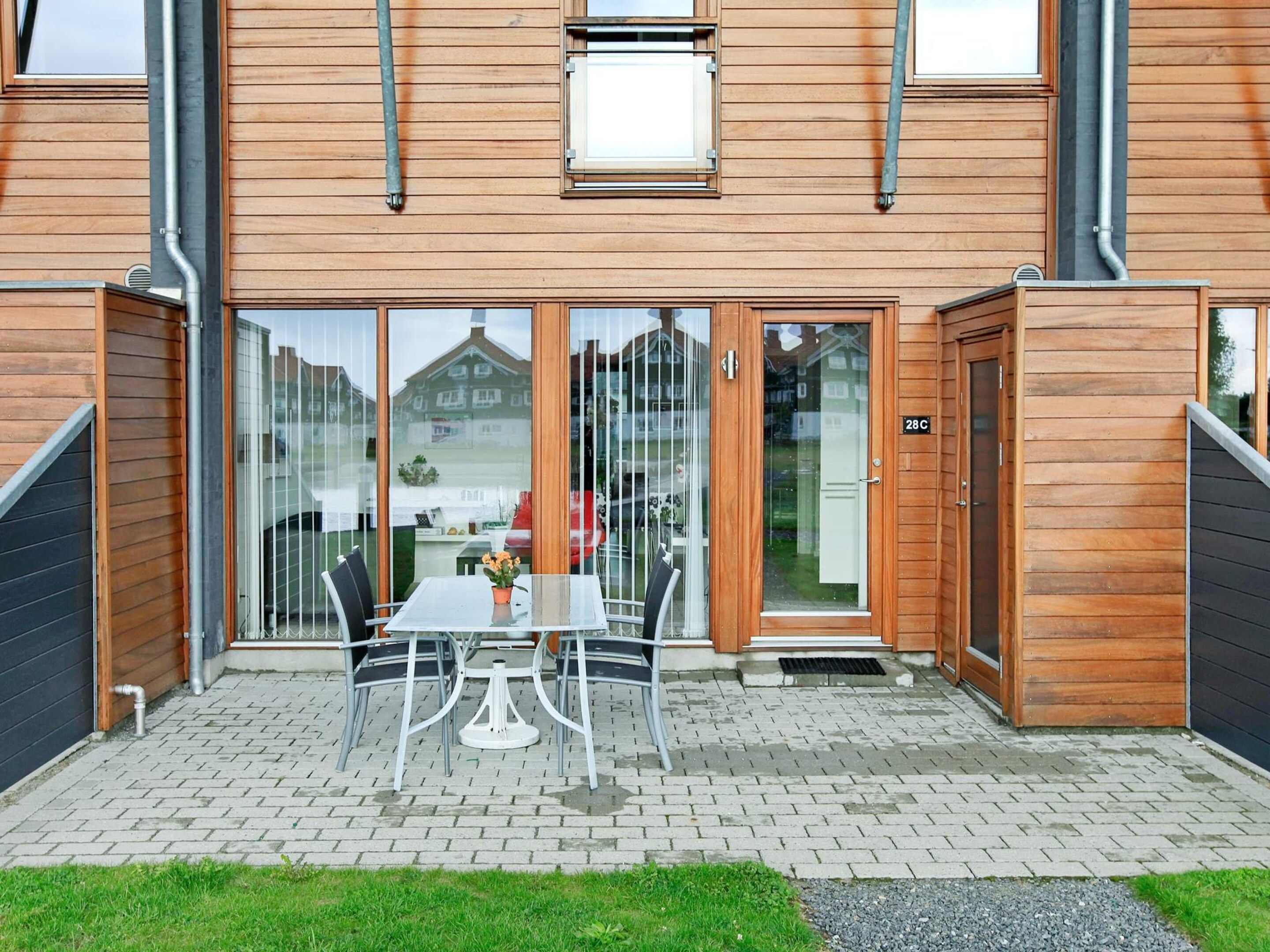 A wooden house with a glass door entrance, a brick patio, and a table with chairs outside.