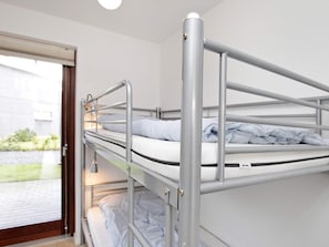 A bunk bed with metal railings and a window with a view of a building and greenery outside.