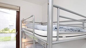 Een stapelbed met metalen spijlen en een raam met uitzicht op een gebouw en groen.