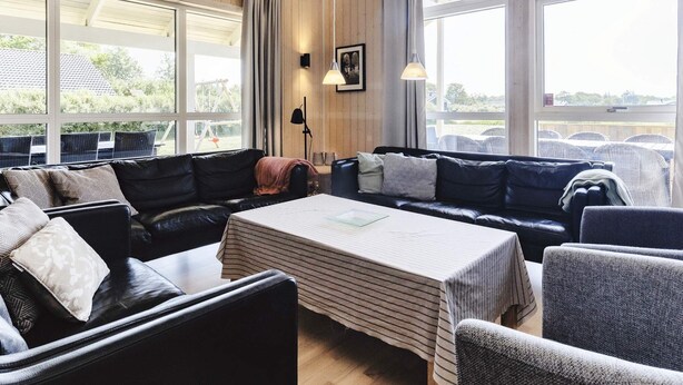 Quarto espaçoso com grande janela, sofá de couro preto, mesa listrada e vista para o exterior.