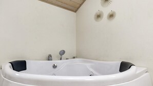 Una bañera blanca independiente con cabezal de ducha y grifo, frente a una pared lisa con techo de vigas de madera.