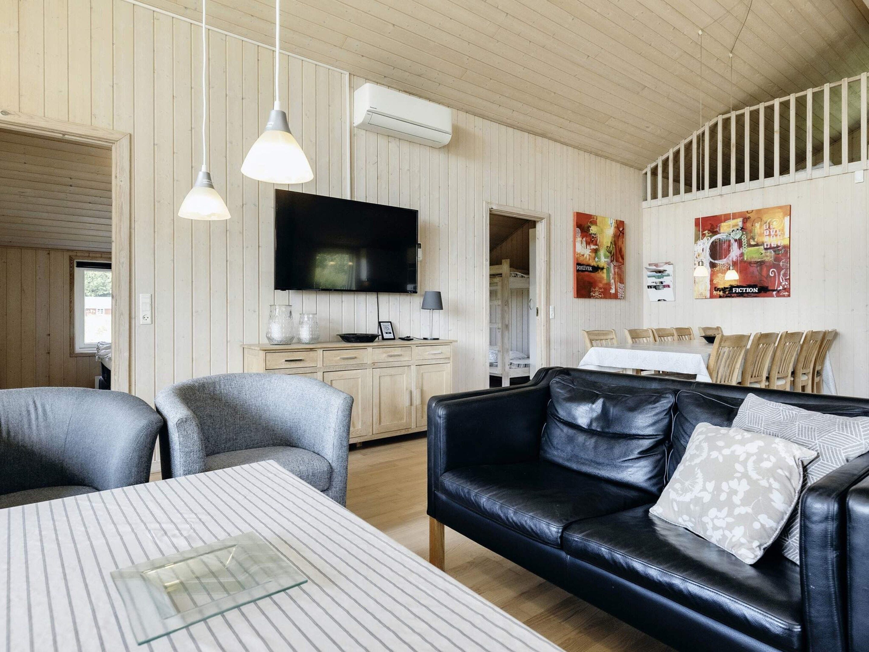 Una sala de estar acogedora con un sofá de cuero negro, una mesa de comedor y un televisor montado en la pared.