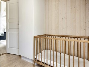 A room with a wooden crib, white walls, and a wooden floor.