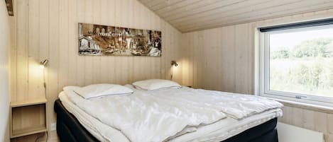 Un dormitorio con cama, paredes de madera, una ventana y un cuadro.
