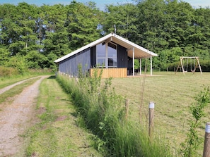 A single-story building with a covered porch and a swing set in a grassy field.