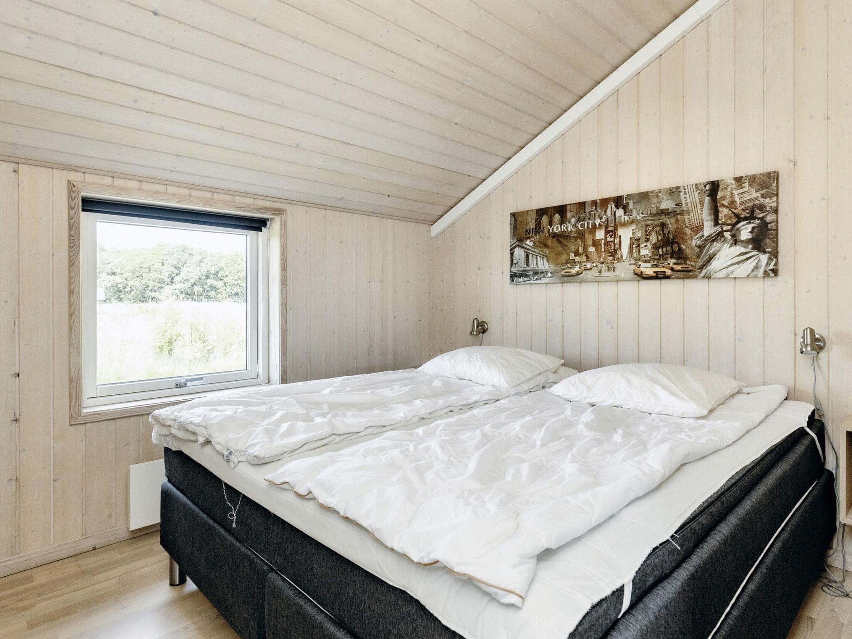 A bedroom with a bed, a window, and a wall-mounted artwork.