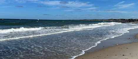 A beach with waves, a clear sky, and a distant rocky shoreline.