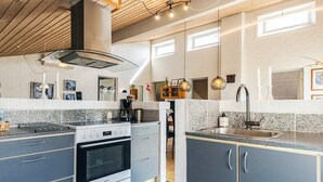 A modern kitchen with a built-in oven, a stove, and a sink. There are hanging lights and a window above the sink. - 7 Person Holiday Home in Thisted (Thisted)