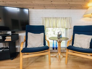 A living room with two blue armchairs, a small round table, a TV, and a window with curtains.