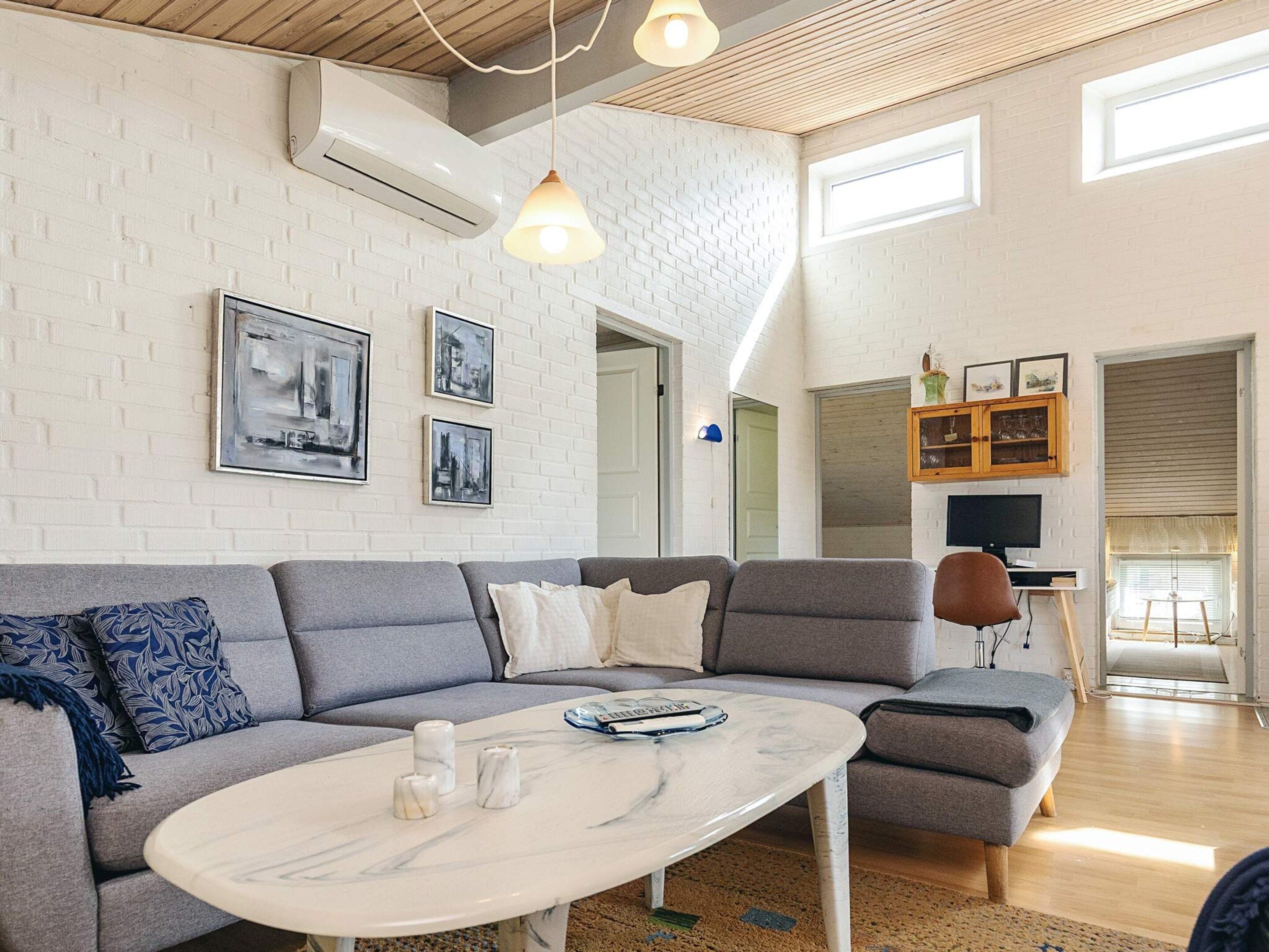 A modern living room with a grey sectional sofa, a marble coffee table, and a white brick wall with framed artwork.