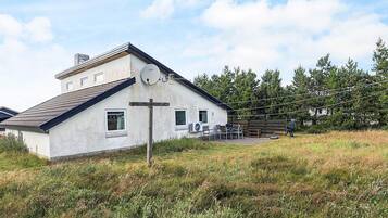 Une maison de plain-pied avec un toit en pente, une antenne parabolique et un petit porche aménagé avec du mobilier d’extérieur.