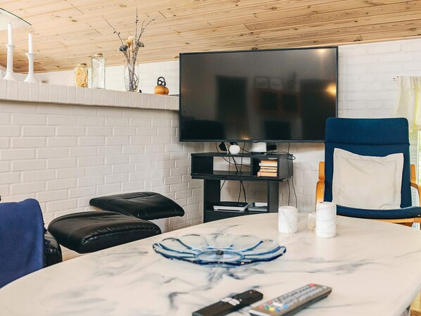 A living room with a flat-screen TV, a blue chair, a white table with a marble top, and a black leather sofa.