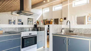 Une cuisine moderne équipée d’un four encastré, d’une cuisinière et d’un évier. Des luminaires suspendus et une fenêtre au-dessus de l’évier complètent l’ensemble.