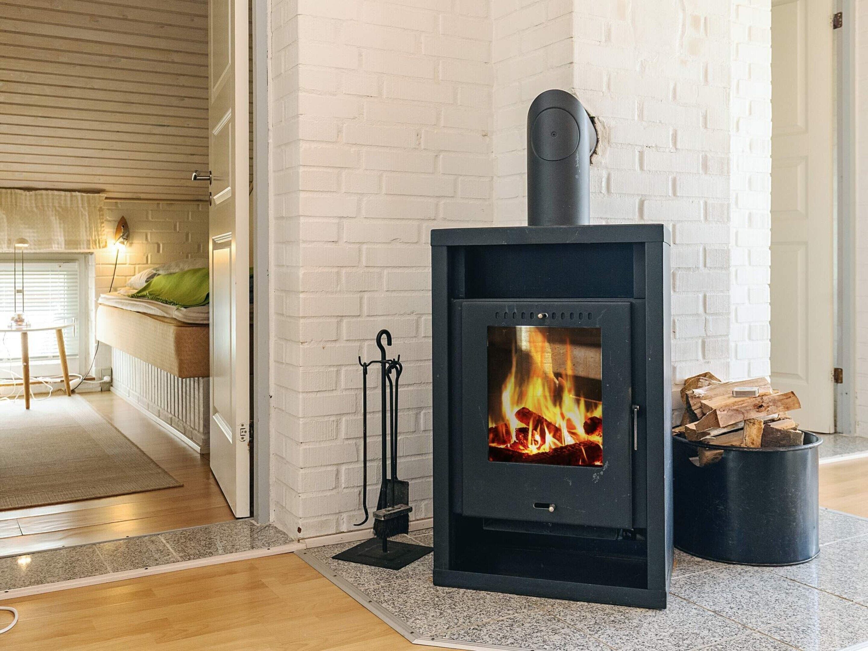 Una sala de estar moderna con un estufa de leña negra, paredes de ladrillo blanco y una zona de estar acogedora con un cojín verde.