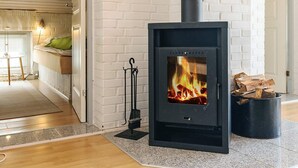 A modern living room with a black wood-burning stove, white brick walls, and a cozy seating area with a green cushion. - 7 Person Holiday Home in Thisted (Thisted)