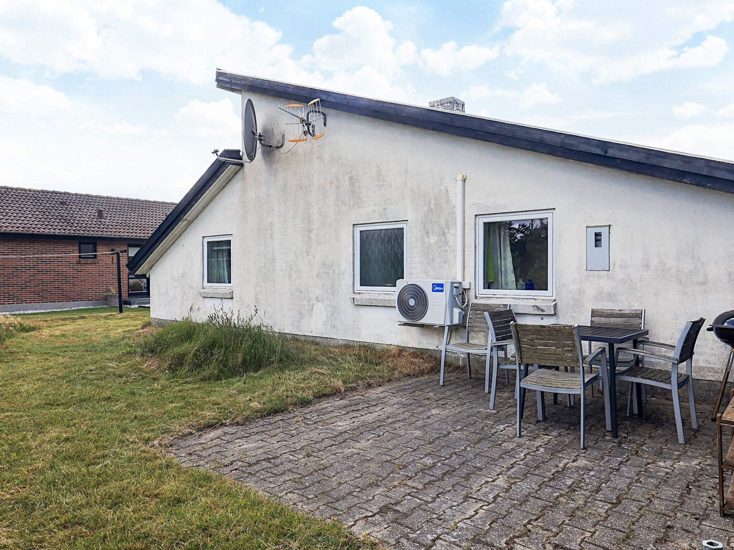 Ein Wohngebäude mit Backsteinfassade, einer Satellitenschüssel und einer Terrasse mit Gartenmöbeln.