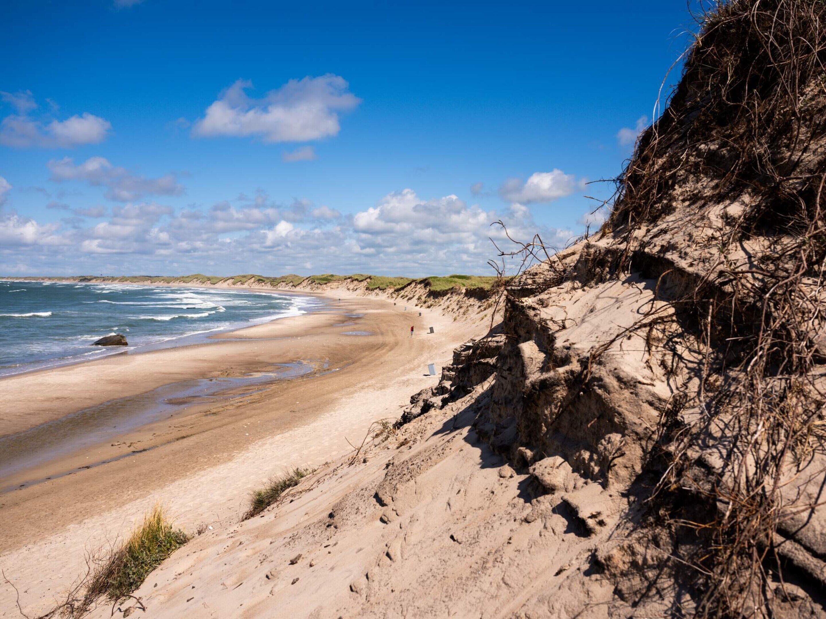 Een zandstrand met golven, een heldere lucht en een rotsachtige klif.