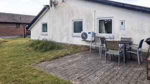 Una casa con fachada de ladrillo, antena parabólica y un patio con sillas y una mesa.
