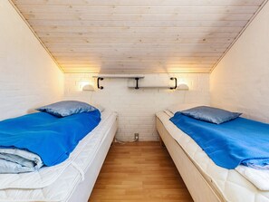 A small, cozy room with two single beds, wooden ceiling, white brick walls, and a wooden floor.
