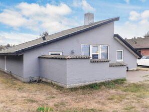A single-story building with a grey exterior, a pitched roof, and a small window with a shutter.