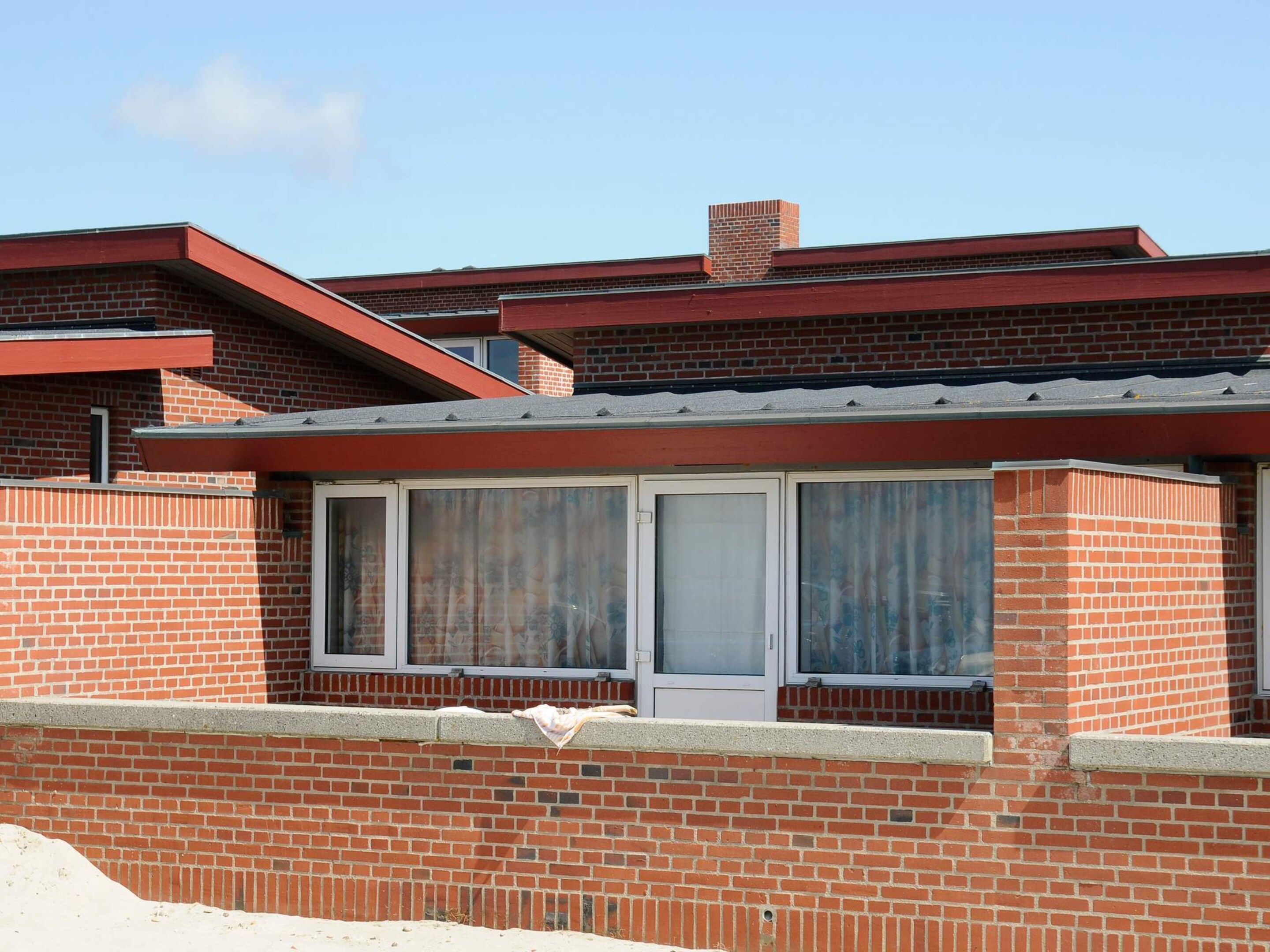 A single-story brick building with a flat roof, a chimney, and a window with curtains.