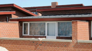 A single-story brick building with a flat roof, a chimney, and a window with curtains. - 6 Person Holiday Home in Henne (Henne)