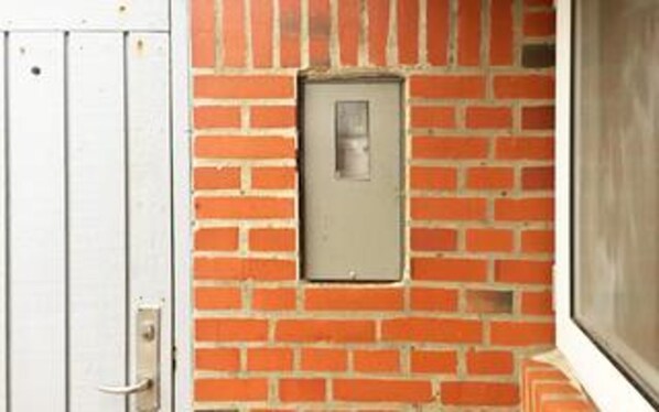 Un mur de briques avec une boîte électrique rectangulaire et une porte.