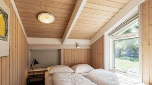 A bedroom with a wooden ceiling, a bed with white bedding, a desk with a lamp, and a window with a view of greenery. - Luxury Retreat Near Beach - By Traum Ferienwohnungen (Otterup)