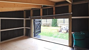 A room with a large open door leading to a fenced outdoor area, wooden flooring, and a green recycling bin. - Luxury Retreat Near Beach - By Traum Ferienwohnungen (Otterup)