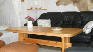 A cozy living room with a black leather sofa, a wooden coffee table with a vase of pink flowers, and a fur rug hanging on the wall. - 4 Person Holiday Home in Jerup-by Traum (Jerup)