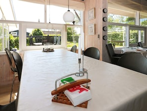 Un espace repas avec une longue table, des chaises, des luminaires suspendus et une vue dégagée grâce à de grandes fenêtres.