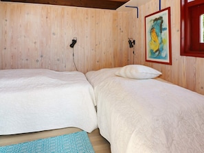 Una habitación con dos camas, paredes de madera, un cuadro y un ventanal con detalles rojos.