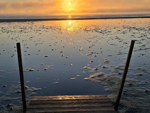 A wooden pier extending into a calm body of water with a sunset in the background.