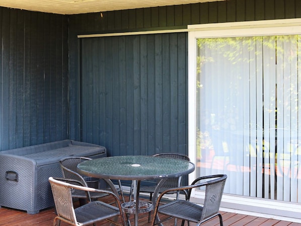 Un patio couvert comprenant une table ronde et quatre chaises, un canapé et une porte-fenêtre coulissante.