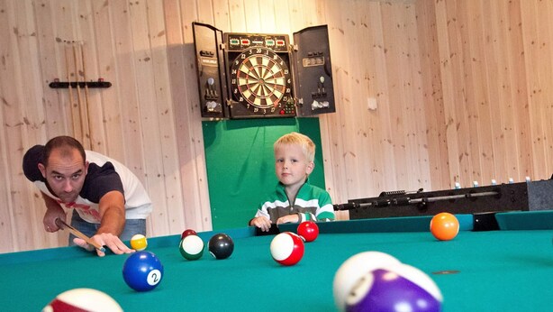 Ein Billardtisch mit Kugeln und ein Dartboard im Hintergrund.