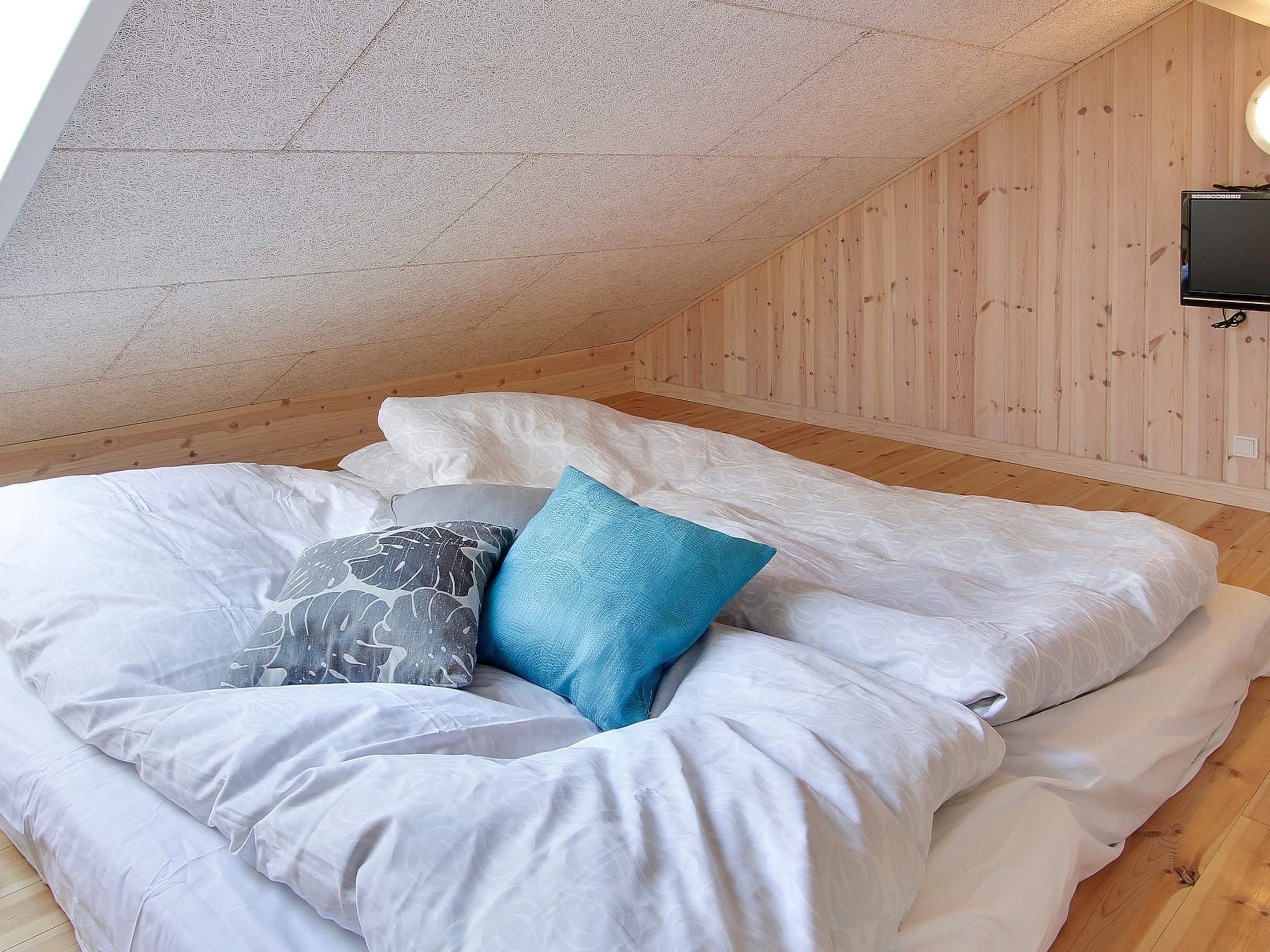 A bedroom with a sloped ceiling, wooden walls, a bed with white bedding and patterned pillows, and a mounted television.