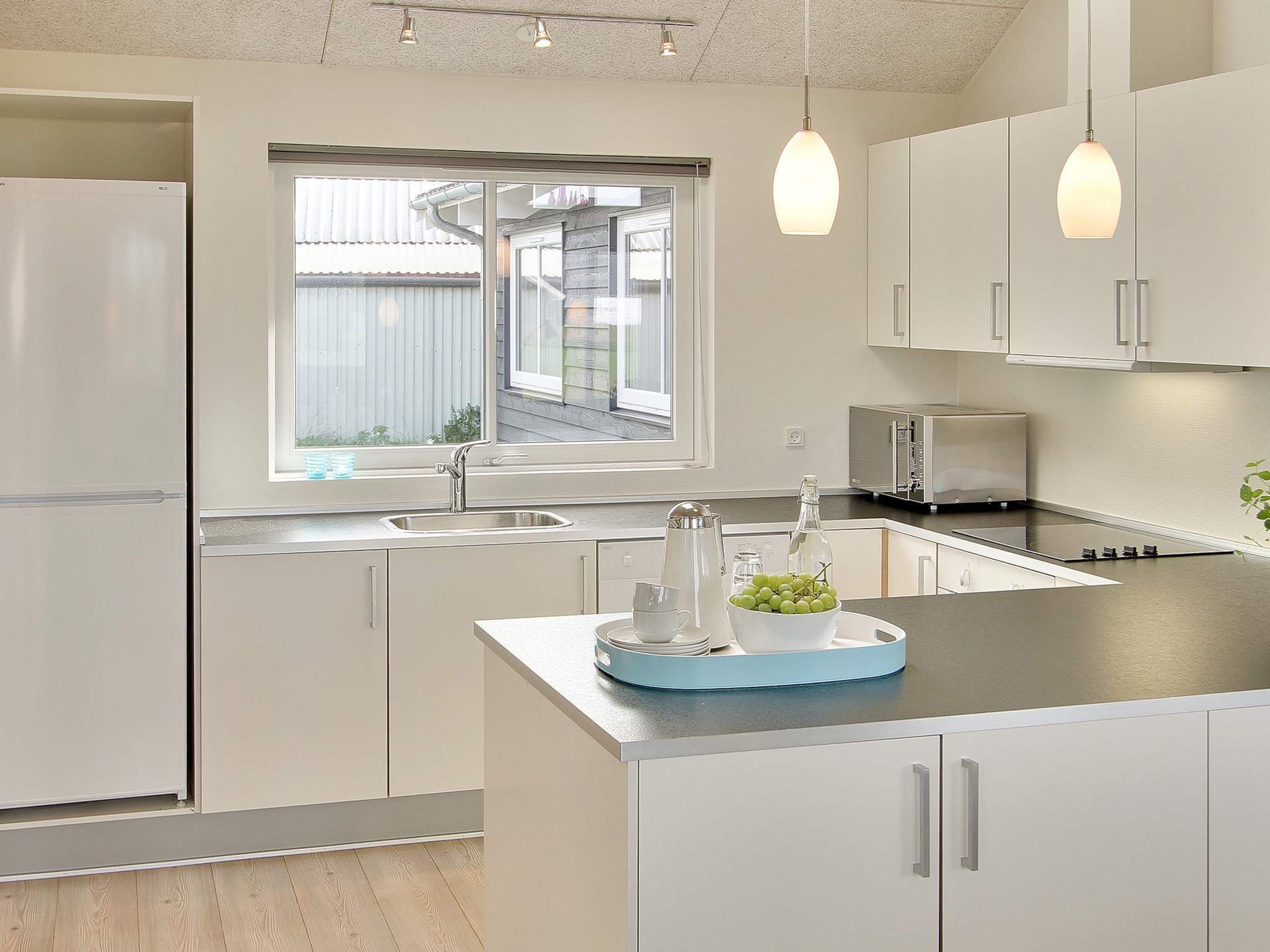 Una cocina moderna con armarios blancos, horno empotrado, lavamanos y ventana con vistas al exterior.