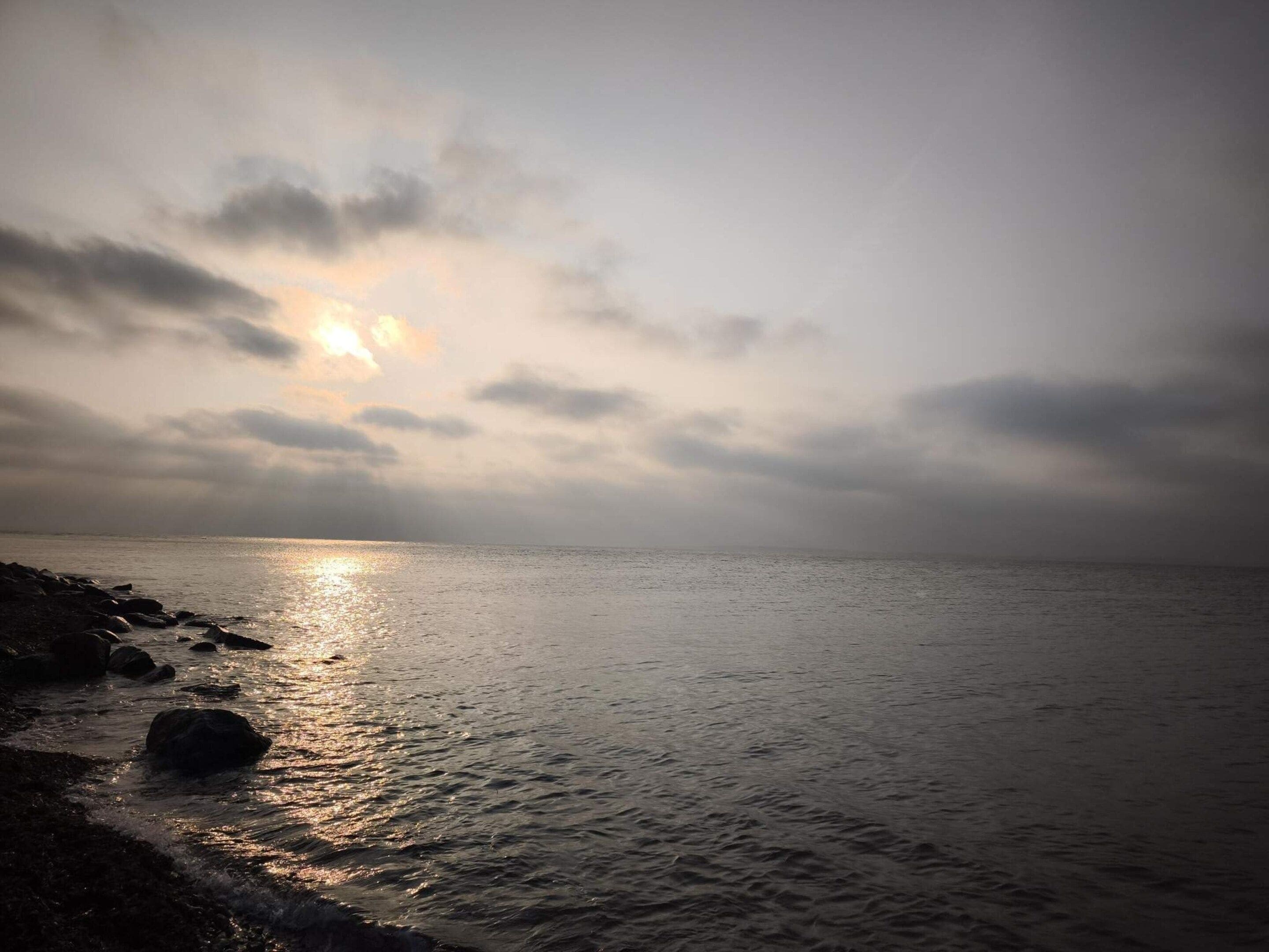 Ruhige See mit felsiger Küste und bewölktem Himmel.
