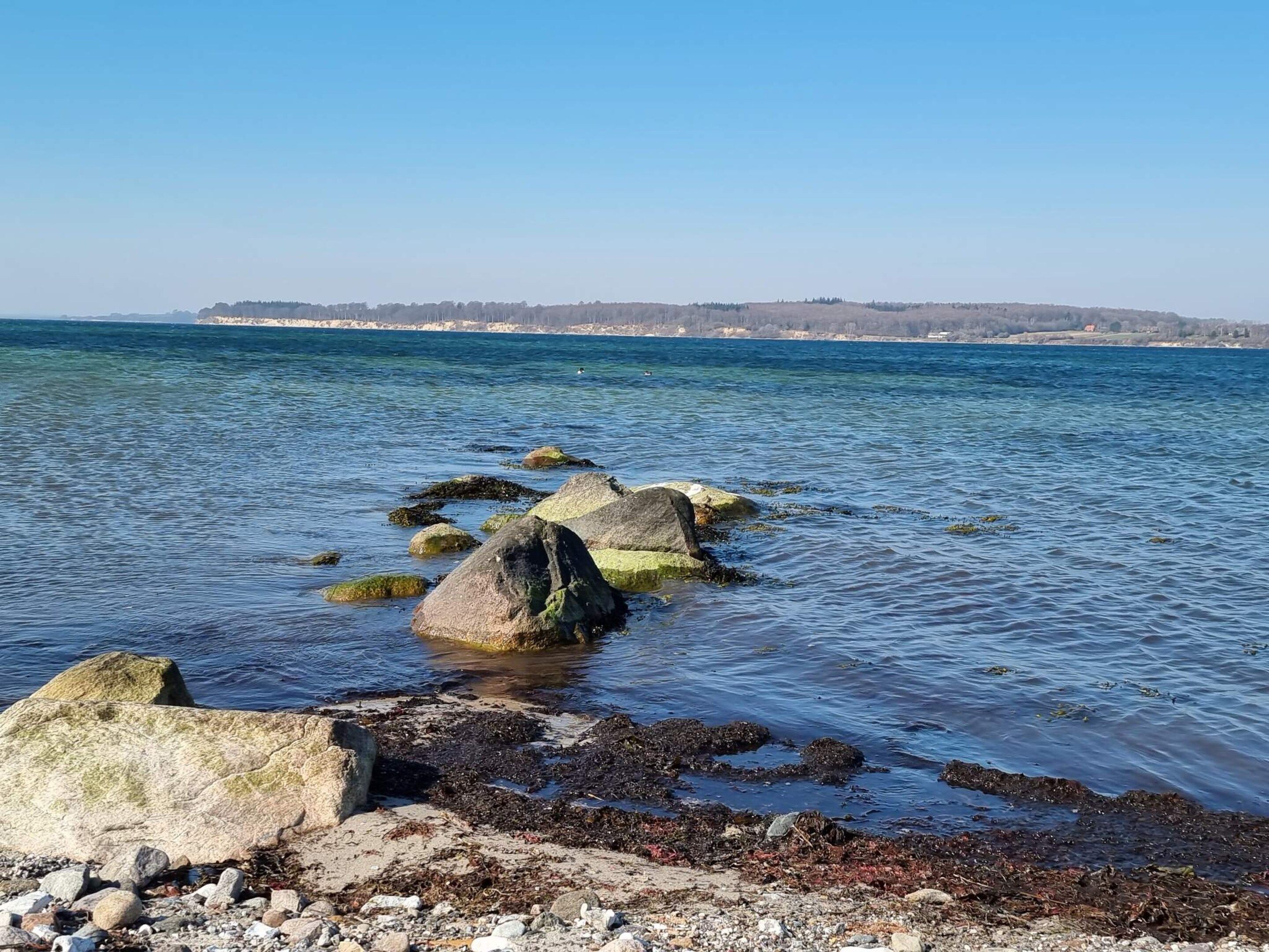 A coastal landscape with clear water, rocks, and a distant shoreline.