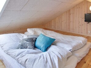 A bedroom with a sloped ceiling, wooden walls, and a bed with white bedding and patterned pillows. - 5 Star Holiday Home in Sydals (Sydals)