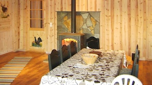 A log cabin interior with a fireplace, wooden walls, a dining table, and chairs. - 9 Person Holiday Home in Bjelland (Lindesnes)