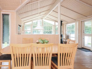 Un coin repas en bois, avec une table et des chaises, de grandes fenêtres et un luminaire suspendu.