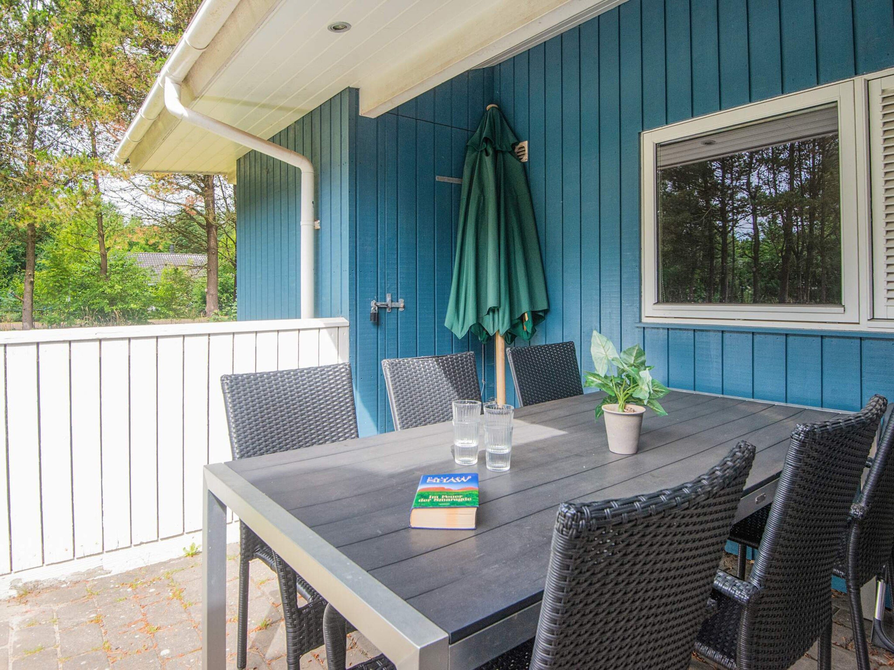 A covered patio with a table and chairs, a potted plant, and a book.