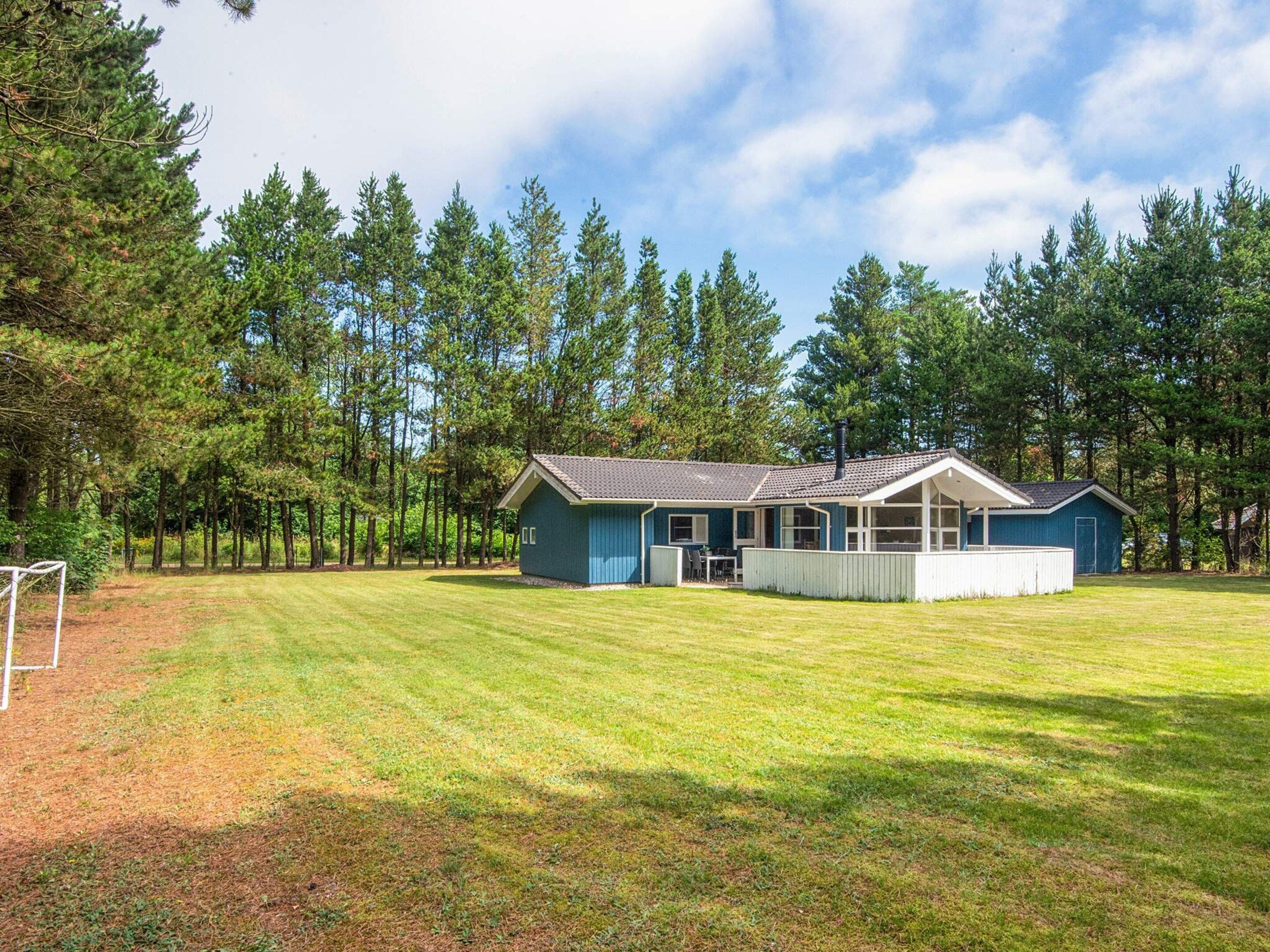 A single-story house with a covered porch, surrounded by a well-maintained lawn and tall trees.