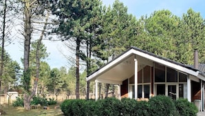 Una casa de planta baixa amb un porxo cobert, envoltada d'un jardí ben cuidat i arbres densos.