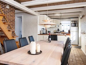 A dining area with a wooden table, black chairs, and candles. A kitchen with a microwave and refrigerator is visible in the background.