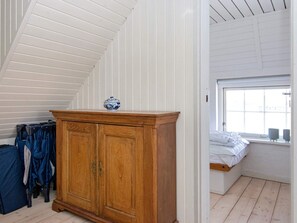 Une pièce avec un plafond en pente, un meuble en bois sur lequel est posé un bol décoratif, un lit avec une literie blanche et une fenêtre offrant une vue.