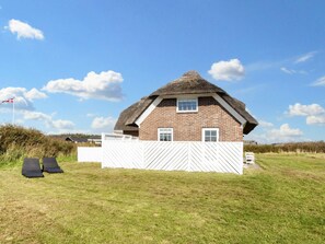 Casa con techo de paja, cerca blanca, una bandera y dos sillones negros.