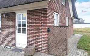 A brick building with a white door and windows, a wooden gate, and a paved pathway. - 9 Person Holiday Home in Harboore (Harboore)