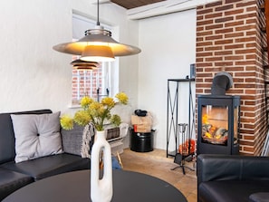 A living room with a sofa, a table with a vase, a fireplace, and a hanging light fixture. - 9 Person Holiday Home in Harboore (Harboore)